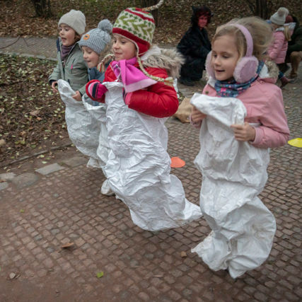 Čtyři veselé malé holčičky skáčou v parku v pytlích.